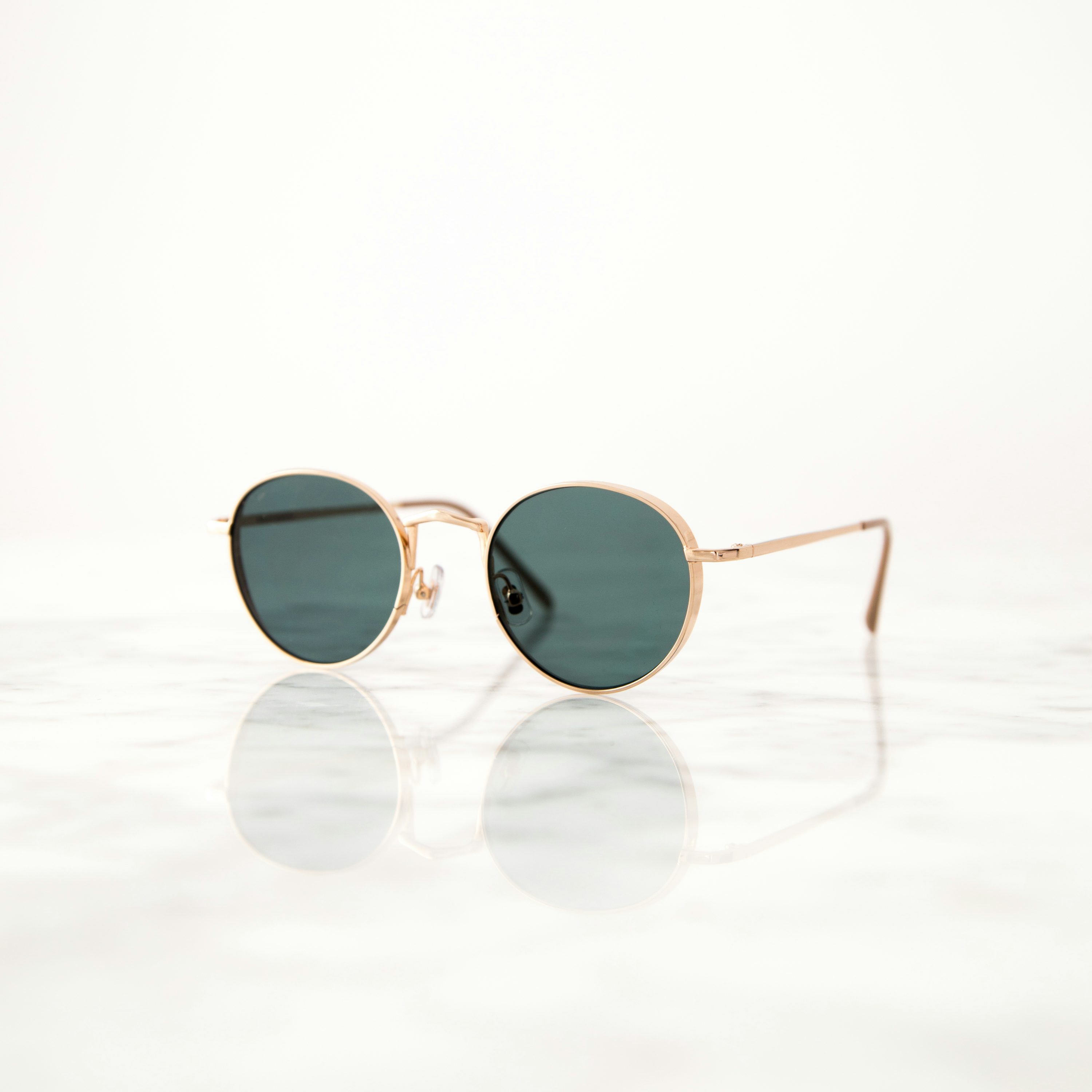Occhiali da sole hippie con montatura color oro su superficie bianca